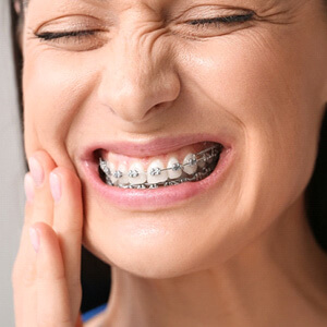 woman with braces pressing her hand to her face in pain