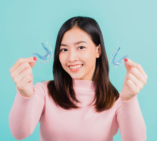 Smiling young woman holding two orthodontic retainers